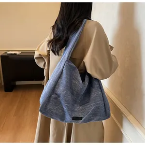 Blue denim tote bag with black leather tag worn over the shoulder with a trench coat
