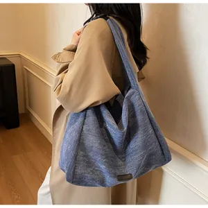 Detail view of blue canvas tote bag on shoulder showing large capacity and leather patch