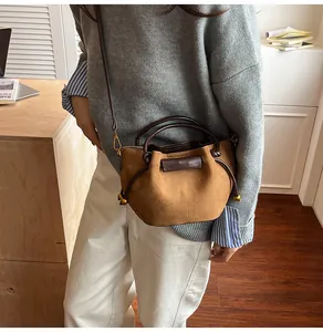 Detail of brown suede bucket bag featuring leather trim and golden metal sphere decor