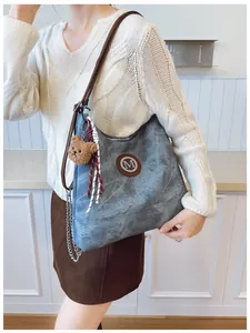 Détail du sac cabas en denim bleu avec logo M en cuir et porte-clés ours en peluche