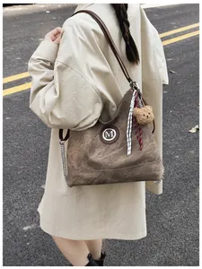 Détail d'un sac cabas marron vintage avec logo M et charme d'ours en plein air
