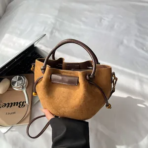 Brown suede drawstring bucket bag with leather handle on a stylish desk setup