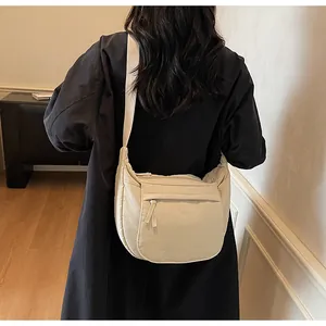 Detail of beige half-moon crossbody bag with front zipper pocket and wide strap on model