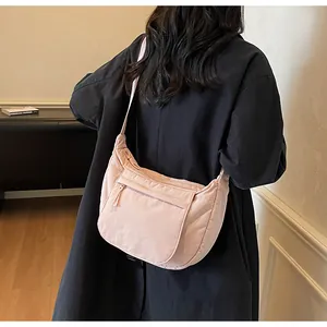 Rear view of a model wearing a light pink nylon crescent bag with adjustable shoulder strap