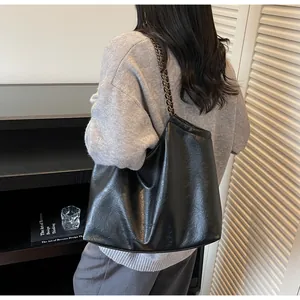 Detail of black leather tote bag featuring chain strap and metallic brand logo accent