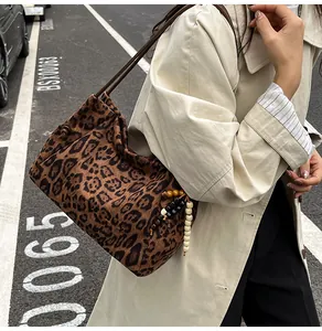 Detail of leopard print suede tote bag with wooden bead charm on a beige trench coat