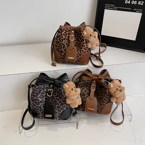 Three leopard print bucket bags with leather trim and bear charms on white steps