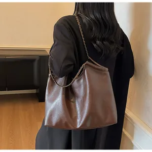Detail of dark brown leather tote featuring chain strap and embossed logo texture