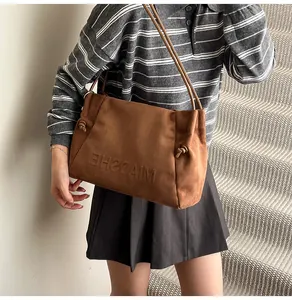 Close-up of brown suede tote bag featuring embossed logo and stylish knotted rope strap