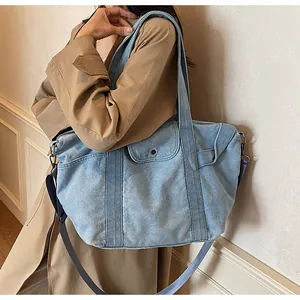 Detail of light blue denim tote bag showing adjustable strap and front flap pocket