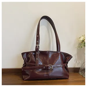 Detail of dark red tote bag featuring silver eyelets and adjustable buckle straps