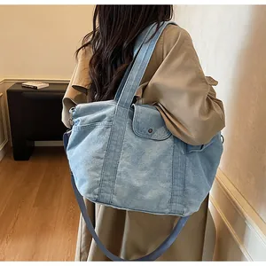 Blue denim tote bag with side pocket and metallic buckle shown with khaki trench coat