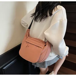 Close-up of coral pink half-moon crossbody bag with adjustable black strap on shoulder