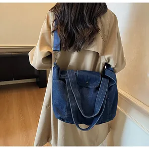 Deep blue denim tote bag with adjustable strap worn over a beige trench coat