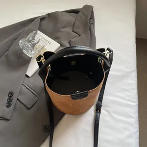 Brown suede bucket bag with black leather trim and adjustable shoulder strap on white bedding