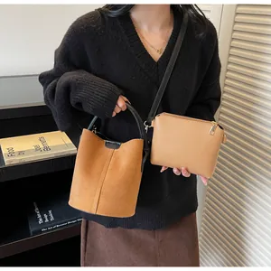 Detail shot of a tan suede bucket bag with round handles and a matching mini crossbody bag