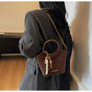 Detail of dark brown matte bucket bag with a round handle and colorful bead charm