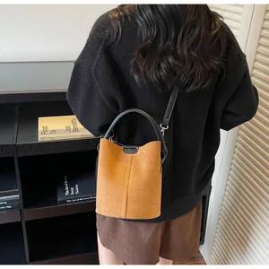 Detail view of brown suede bucket bag featuring decorative stitching and black handles