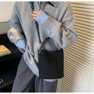 Detail of black suede bucket bag with leather handles shown on model in studio