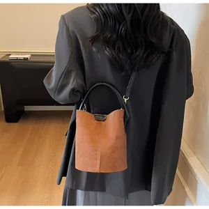 Detail of caramel suede bucket bag with black handles styled with a grey blazer
