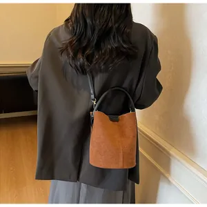 Detail view of a brown suede bucket bag featuring black leather handles and shoulder strap
