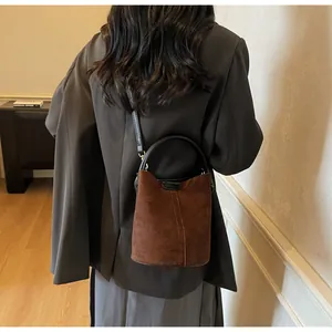 Detailed view of deep brown suede bucket bag with black ring handle and shoulder strap