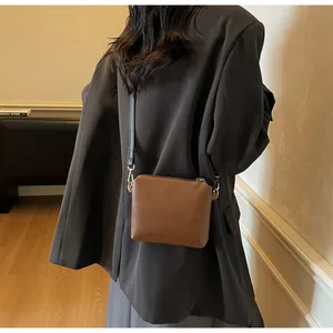Detail of a brown leather crossbody bag with gold hardware worn by a model in a modern room