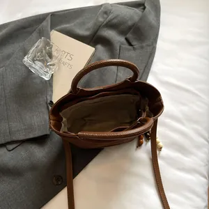 Brown leather bucket tote bag with round handles and wooden bead charm in a soft setting