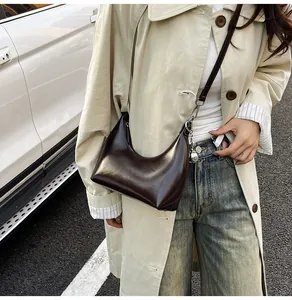 Detail of a dark brown crescent underarm bag with a silver sphere charm on a beige trench coat