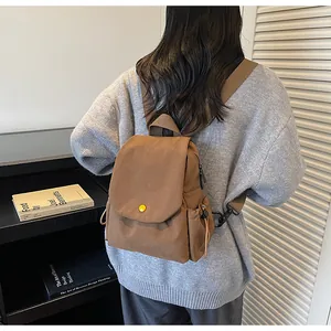 Rear view of model wearing a brown canvas backpack with flap cover and round buckle