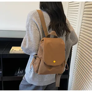 Rear view of a model wearing a brown canvas flap backpack with side drawstring pockets