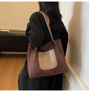 Detail of dark brown suede tote bag with beige leather pocket and silver chain strap