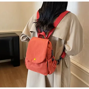Detail of orange canvas backpack showing the side pocket and black metal strap hooks