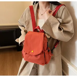 Detail of brick red canvas backpack with yellow button closure and drawstring side pocket