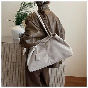 Detail of beige suede tote bag with vertical stitching and decorative charm tag