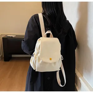 Side view of cream canvas backpack with flap cover and yellow button on female model