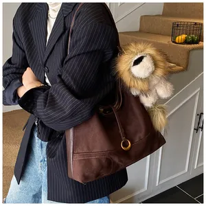 Detail of dark brown matte tote bag with stitching, gold ring, and plush lion pendant