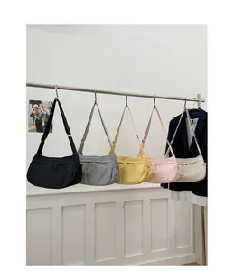 Five nylon crossbody bags in various colors hanging on a metal rack in a minimal studio