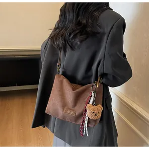 Détail du sac cabas en daim marron avec étiquette cuir, breloque ours et décor de corde