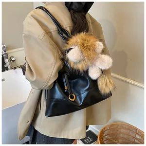 Detail of black matte tote bag with plush lion charm and golden ring hardware accents