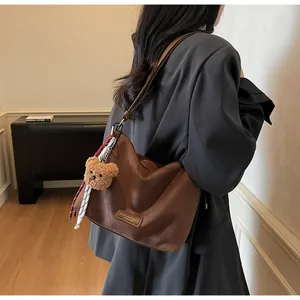Détail du sac cabas en daim marron foncé avec breloque ours en peluche et écusson cuir