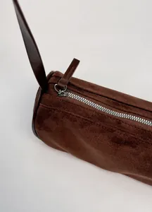 Dettaglio della cerniera metallica e della texture scamosciata marrone della borsa chic