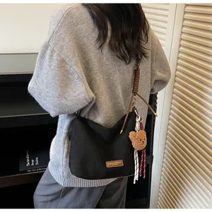 Détail du sac fourre-tout en toile noire avec anses brunes et pendentif ours en peluche