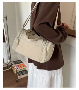 Detailed view of cream-colored cylinder travel bag worn crossbody by a model