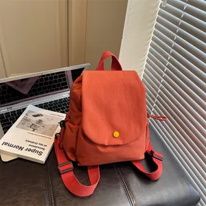 Orange canvas backpack with flap and yellow buckle on desk with books and laptop
