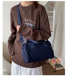 Navy blue nylon travel bag shown on shoulder with adjustable strap and dual handles