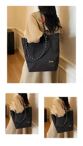 Detail of a large black tote bag featuring a bicolor woven rope strap and yellow brand label