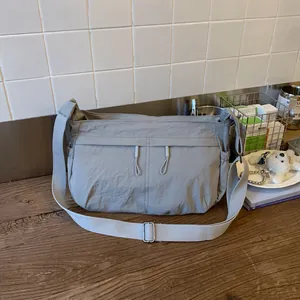 Detail of light gray nylon crossbody bag with dual zipper pockets and wide strap