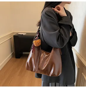 Detailed side view of brown leather hobo bag with teddy charm and striped scarf