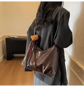 Detail of dark brown leather tote bag with plush bear charm and plaid ribbon accent